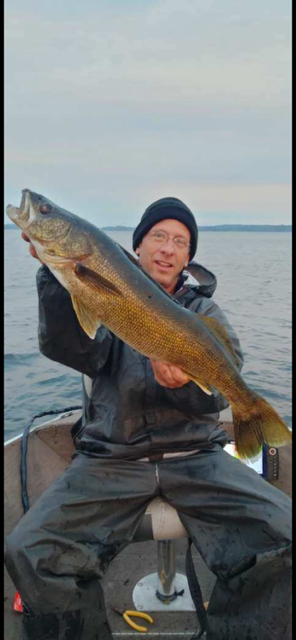 Person on a boat holding up a large fish by calm water at dusk