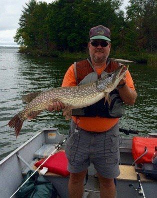 Man holding a large fish on a boat by a wooded lakeshore