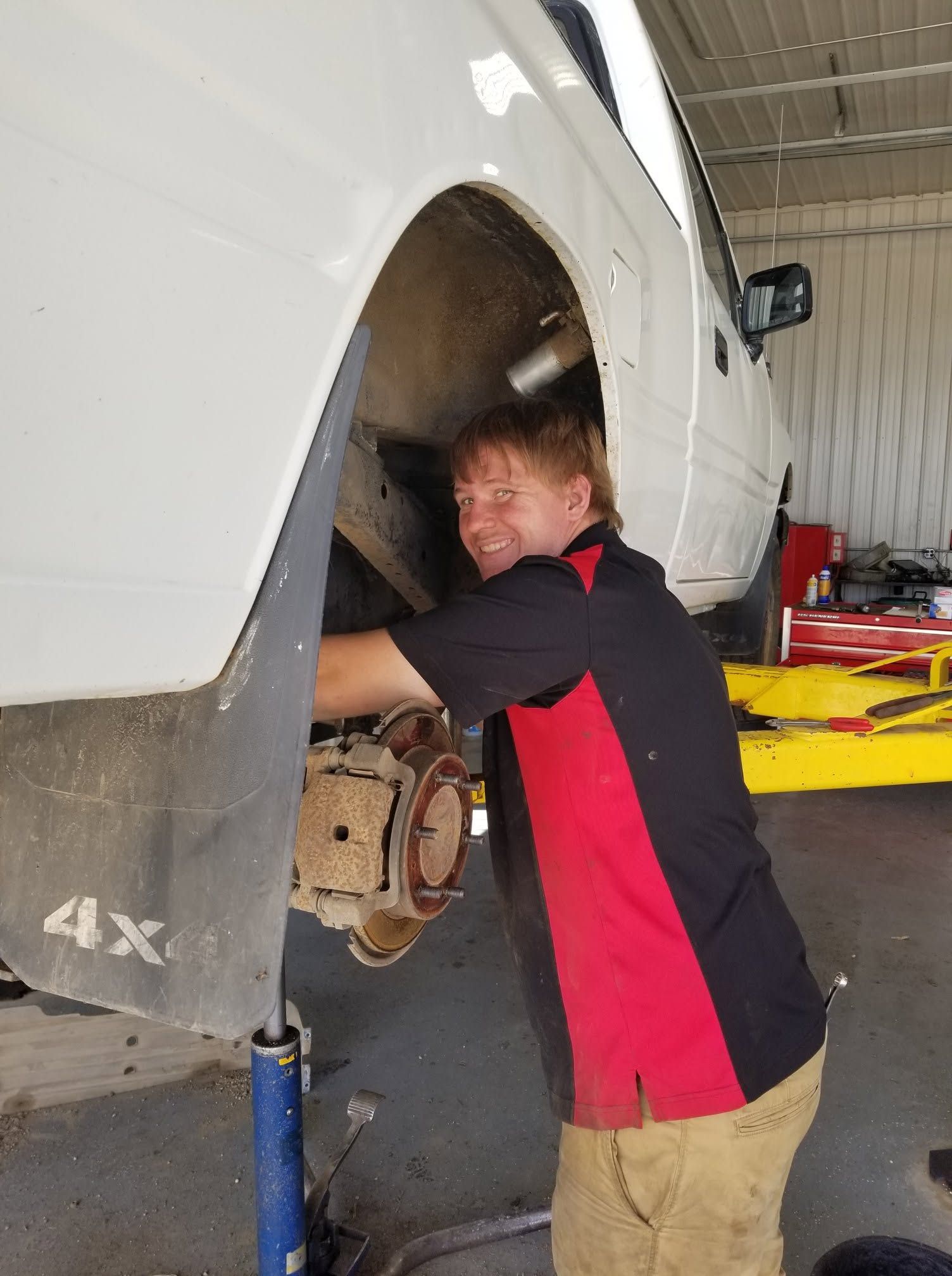 Mechanic working on a white SUV’s exposed front wheel assembly in a garage
