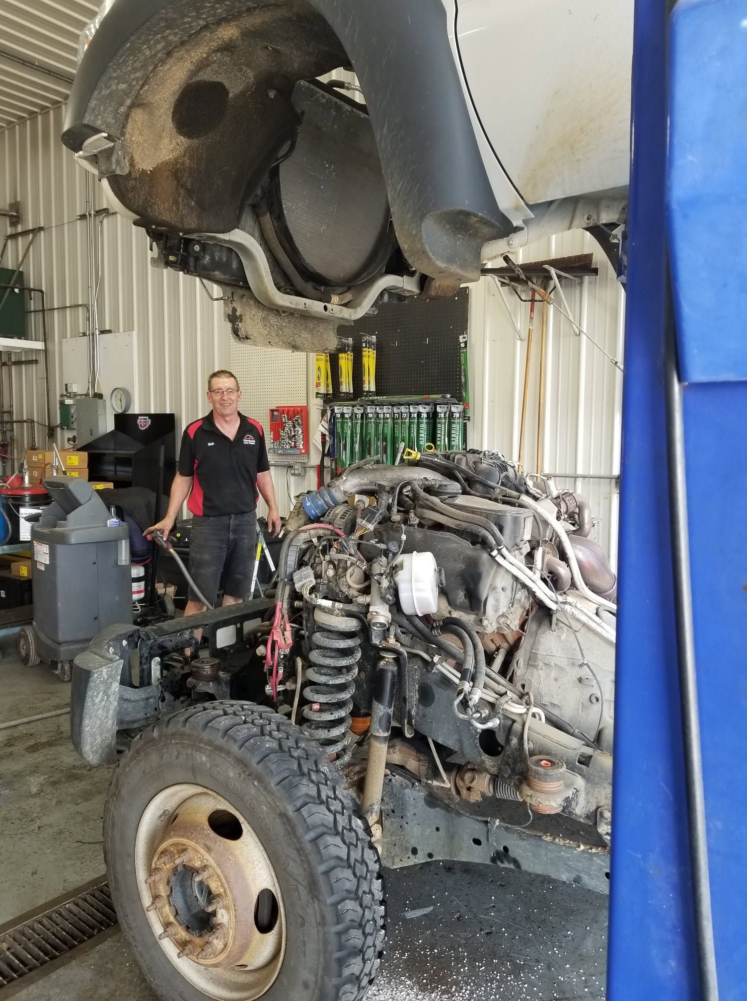 Truck chassis being repaired in a workshop, with a mechanic standing beside it and the cab tilted up. | Scherbenske Auto Repair Inc