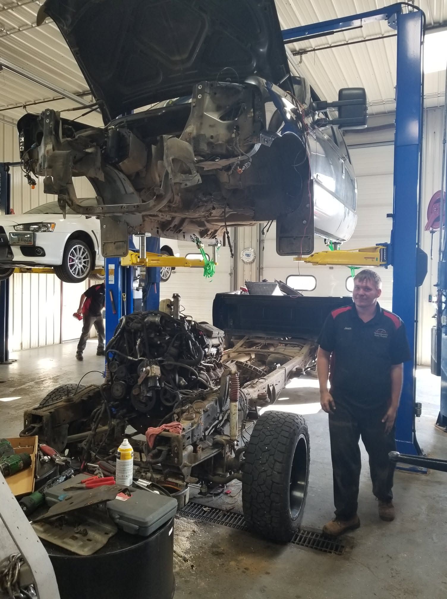 Auto repair shop with a lifted car above a stripped vehicle frame and mechanic standing nearby | Scherbenske Auto Repair Inc