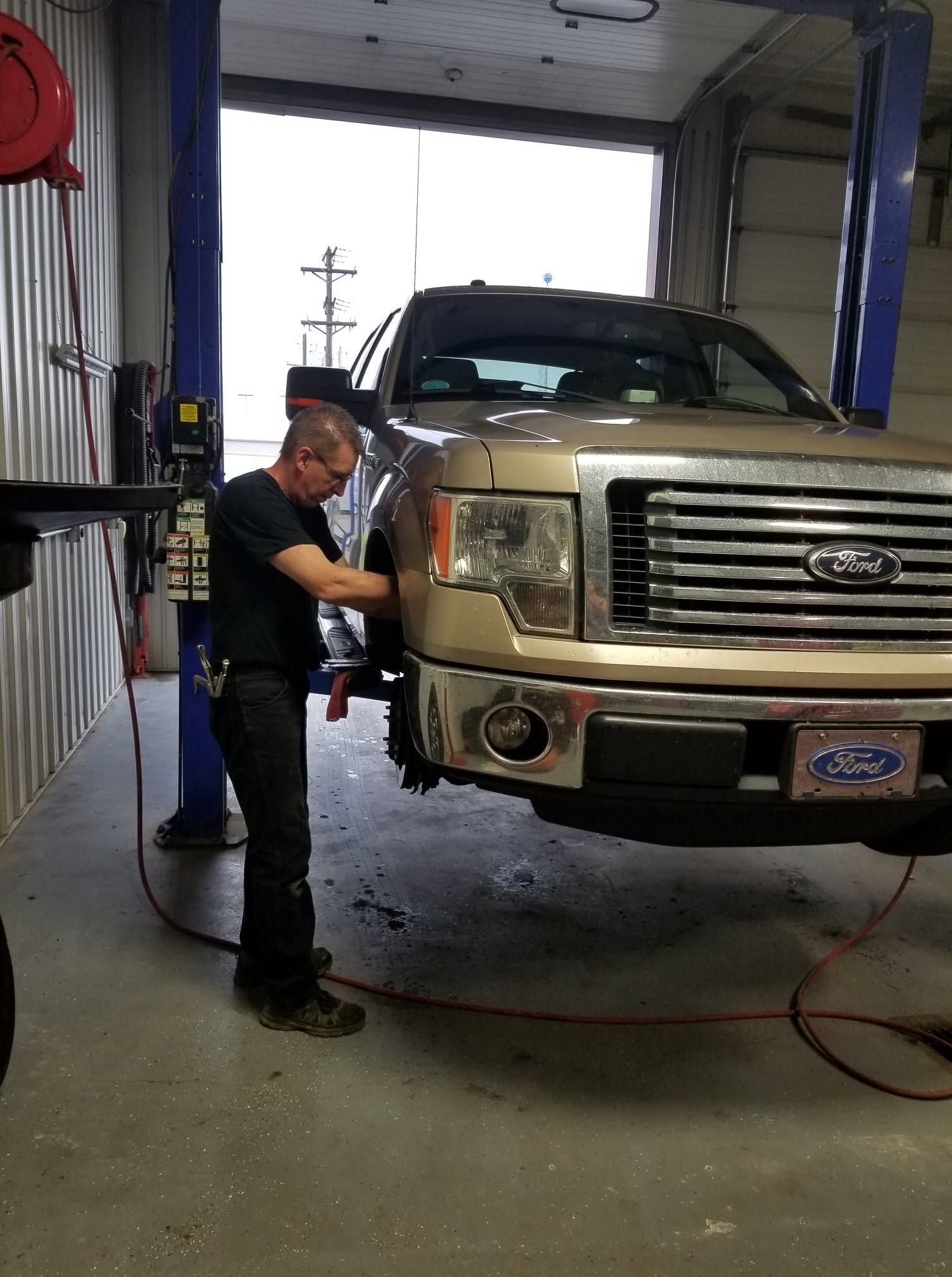 Mechanic working on a white Ford truck inside an auto repair shop | Scherbenske Auto Repair Inc