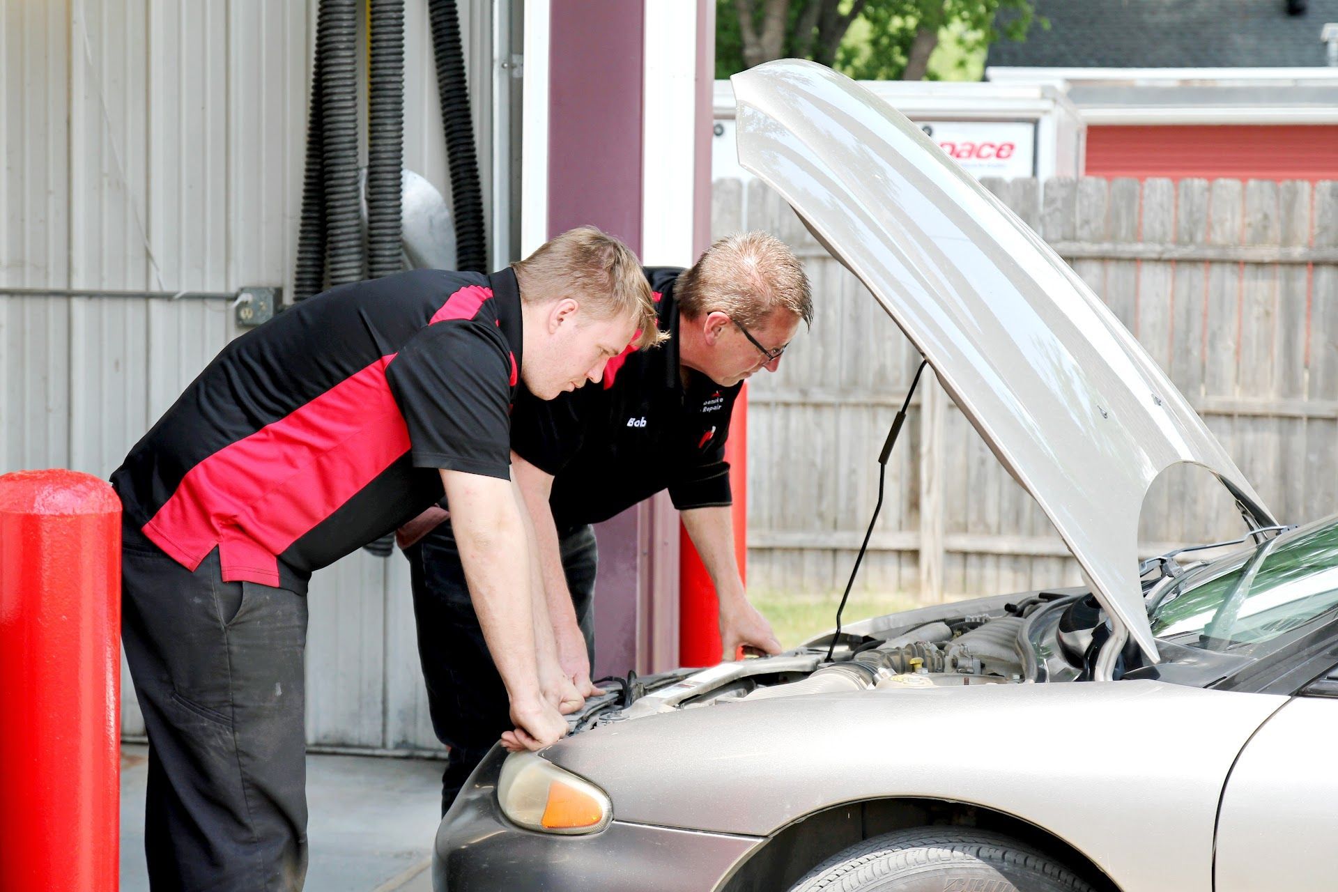 Two mechanics inspecting a white car with its hood open in a garage | Scherbenske Auto Repair Inc