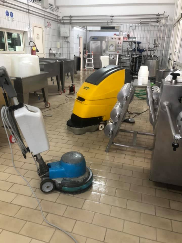 Due macchine lavapavimenti in una cucina industriale piastrellata, una gialla e una blu.