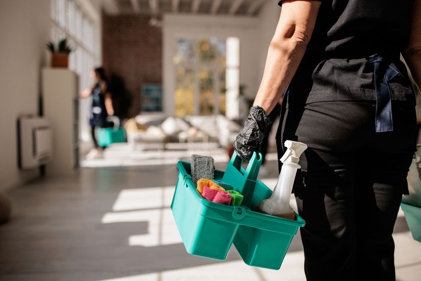 Persona che trasporta un contenitore portatile turchese per le pulizie, con i prodotti al suo interno, in un corridoio luminoso