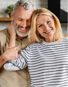A man and a woman are hugging each other and smiling . the woman is wearing a striped shirt.
