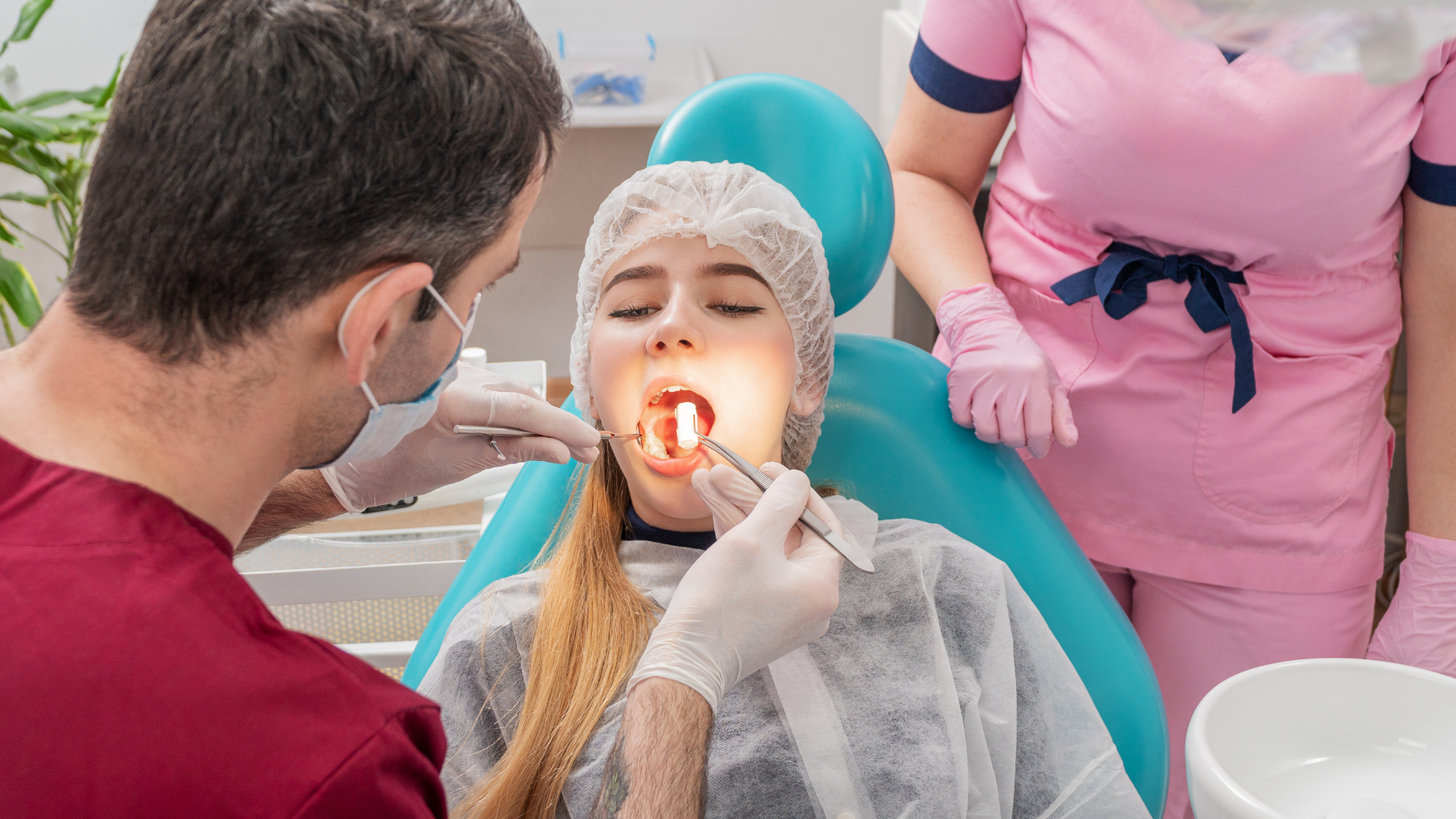 Dental exam with a patient reclined in a chair, dentist using a light in her mouth, assistant nearby