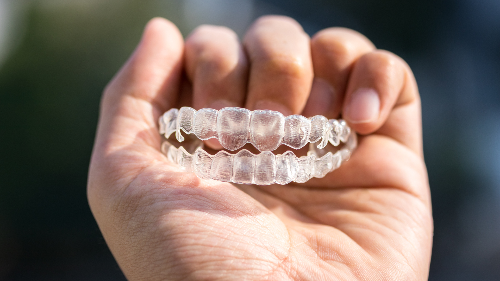 Hand holding a clear dental aligner against a blurred background