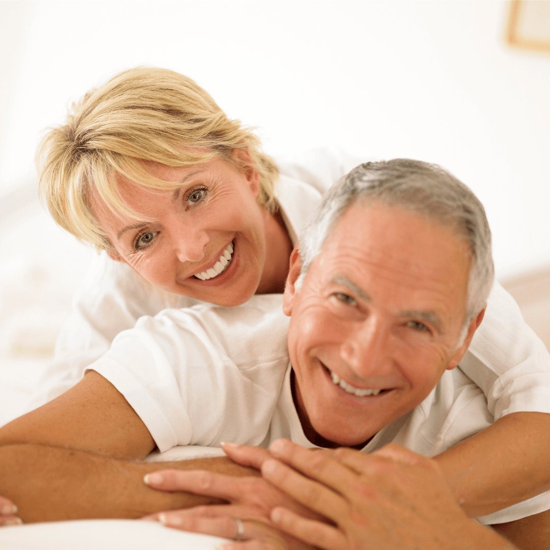 A woman is laying on a man 's back and smiling