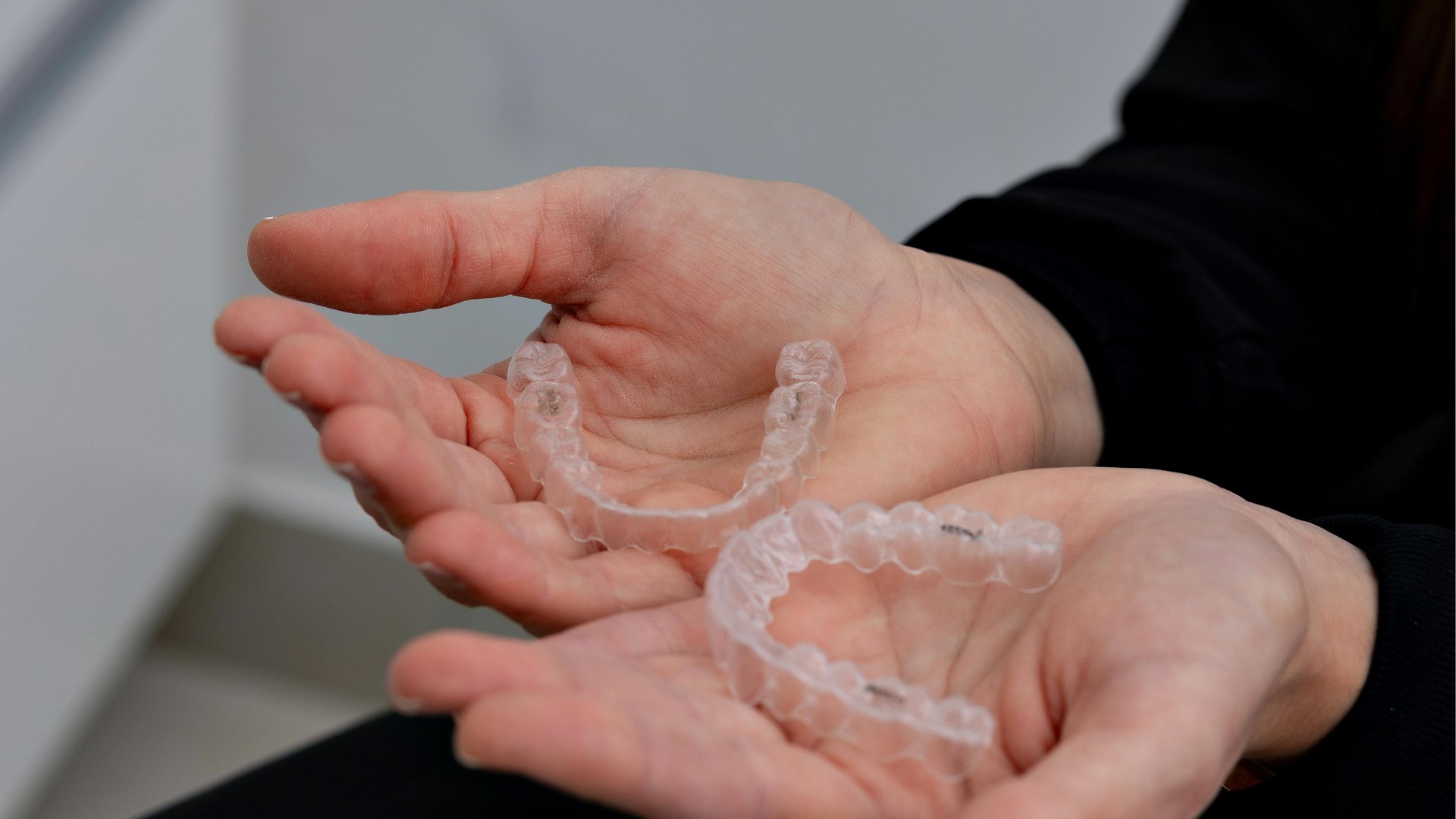 A person is holding two clear braces in their hands.