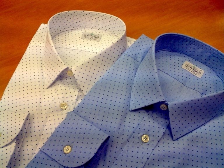 Un uomo con una camicia bianca abbottonata è seduto e guarda di lato, appoggiato a una parete spoglia.