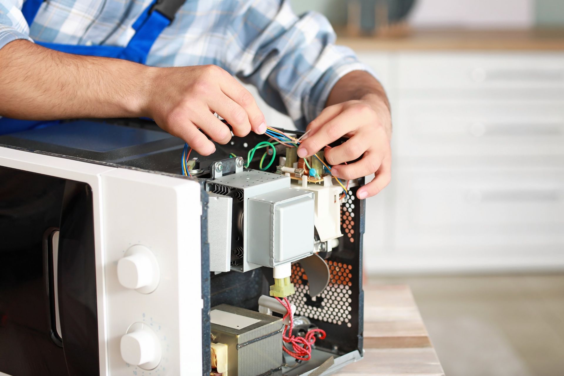 A professional technician in a blue uniform repairing the internal electrical components of an open microwave.