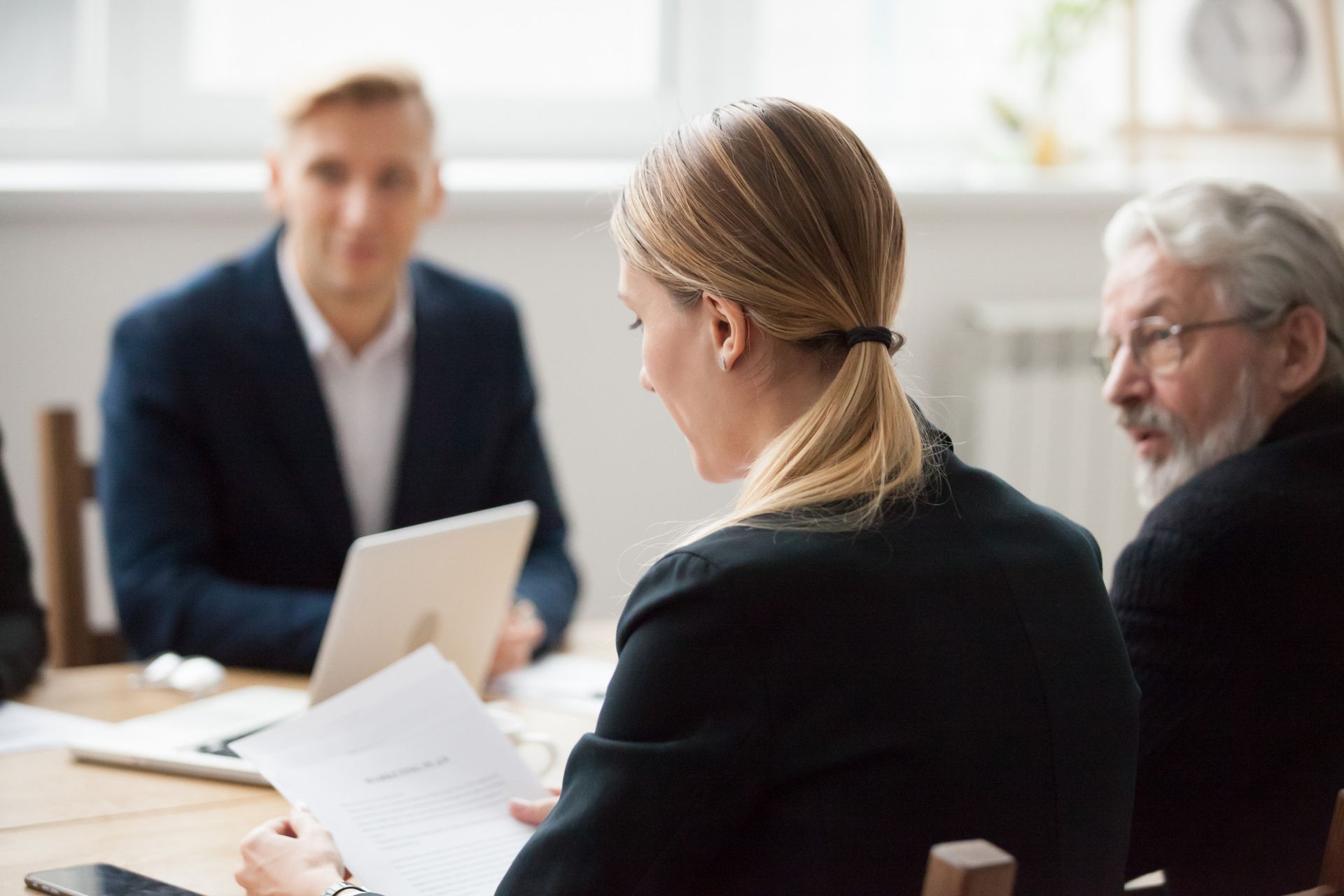 Three people in a meeting, discussing papers around a laptop in a bright office
