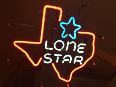 A neon sign shaped like the outline of Texas in orange, with a blue star and the white text