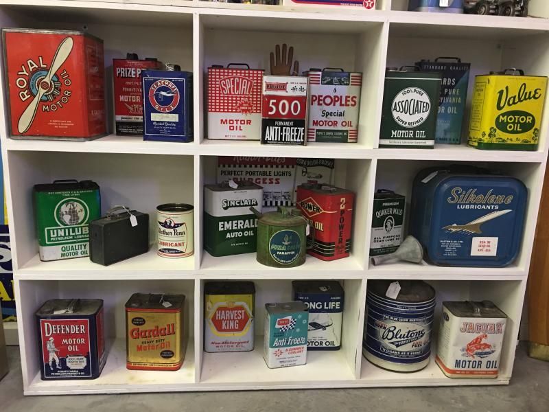 A white shelving unit displaying a collection of vintage, colorful metal motor oil cans and containers.