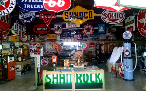 A collection of vintage gas station signs and memorabilia filling a room, with a lit SHAMROCK sign on a front counter.