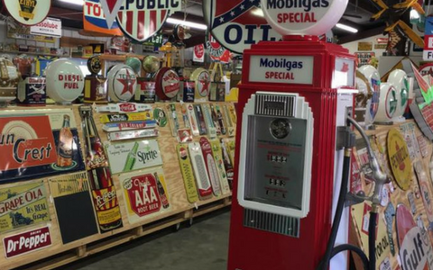 A red Mobilgas gas pump stands in a shop filled with vintage oil signs and advertisements on wooden displays.