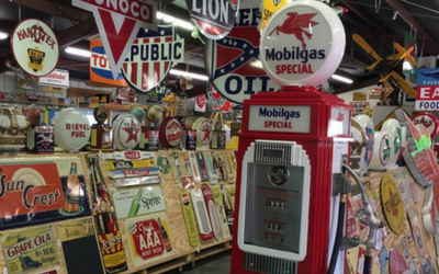 A vintage red Mobilgas fuel pump stands in an antique store filled with colorful retro advertising signs and displays.