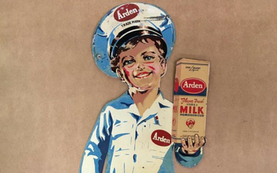 A vintage Arden milk sign showing a smiling person in a blue uniform and cap holding a carton of Arden milk.