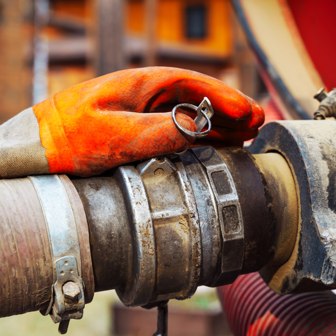 A person wearing an orange glove is holding a hose