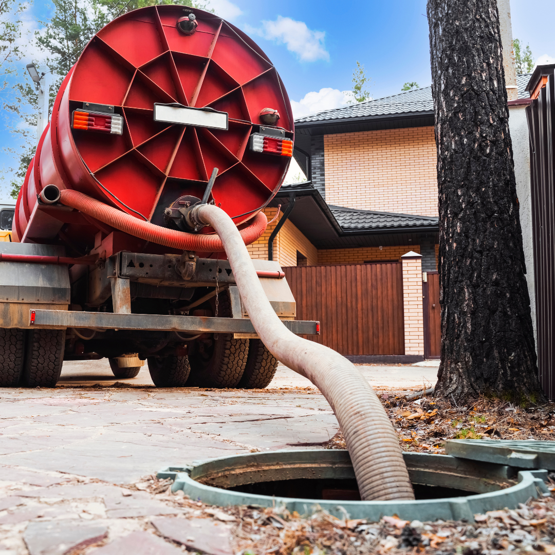A red truck is pumping water into a manhole cover.