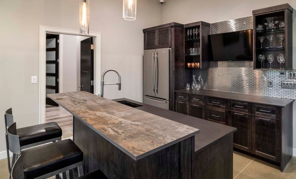A kitchen with a large island , stools , a refrigerator and a television.