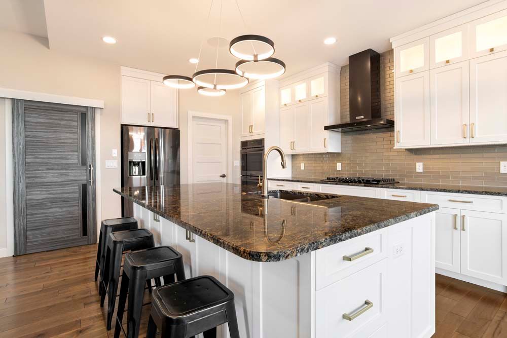 A kitchen with white cabinets , granite counter tops , stools and a large island.