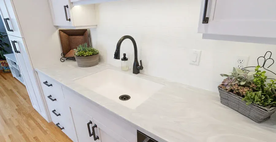 A kitchen with white cabinets and a white sink with a black faucet.