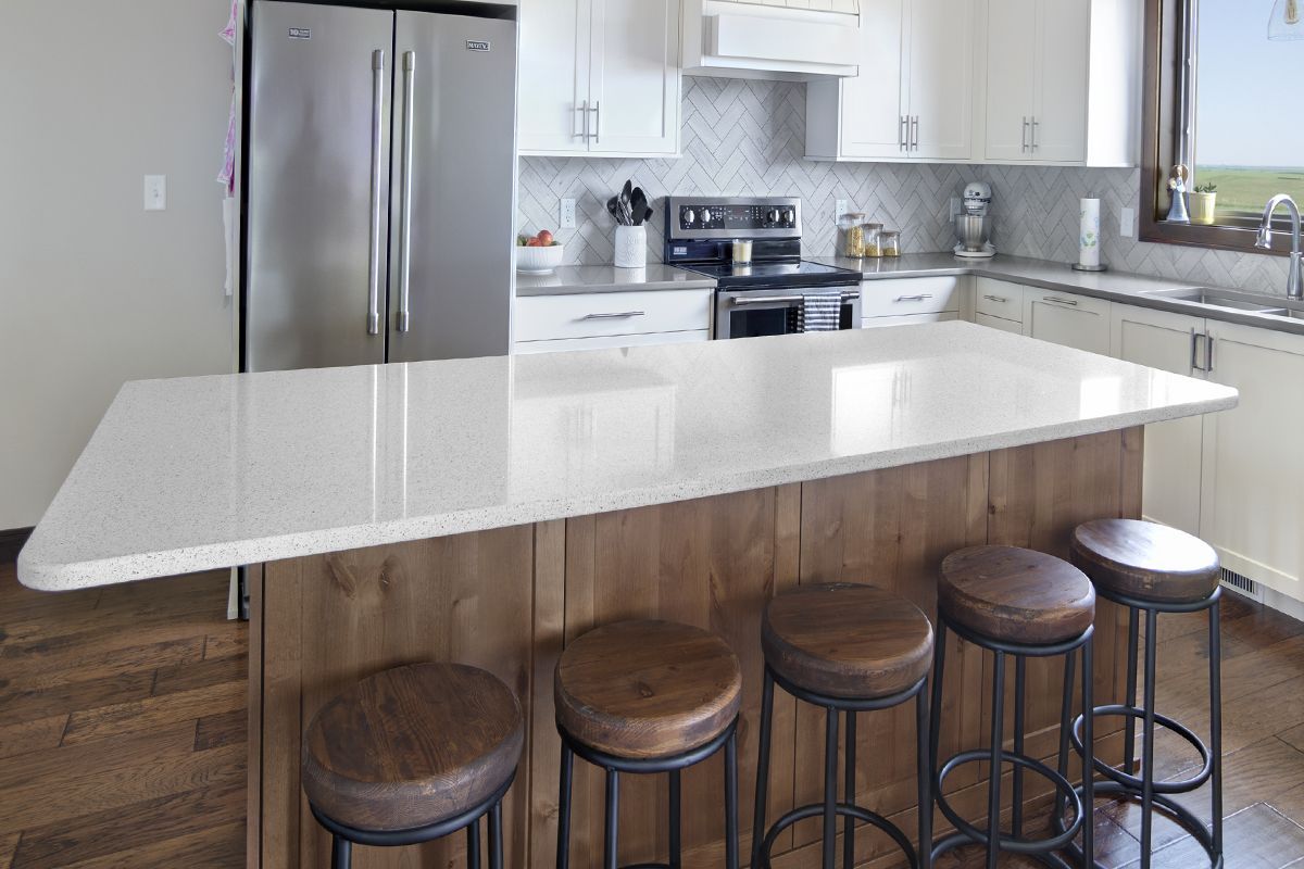 A kitchen with a large island , stools and a refrigerator.