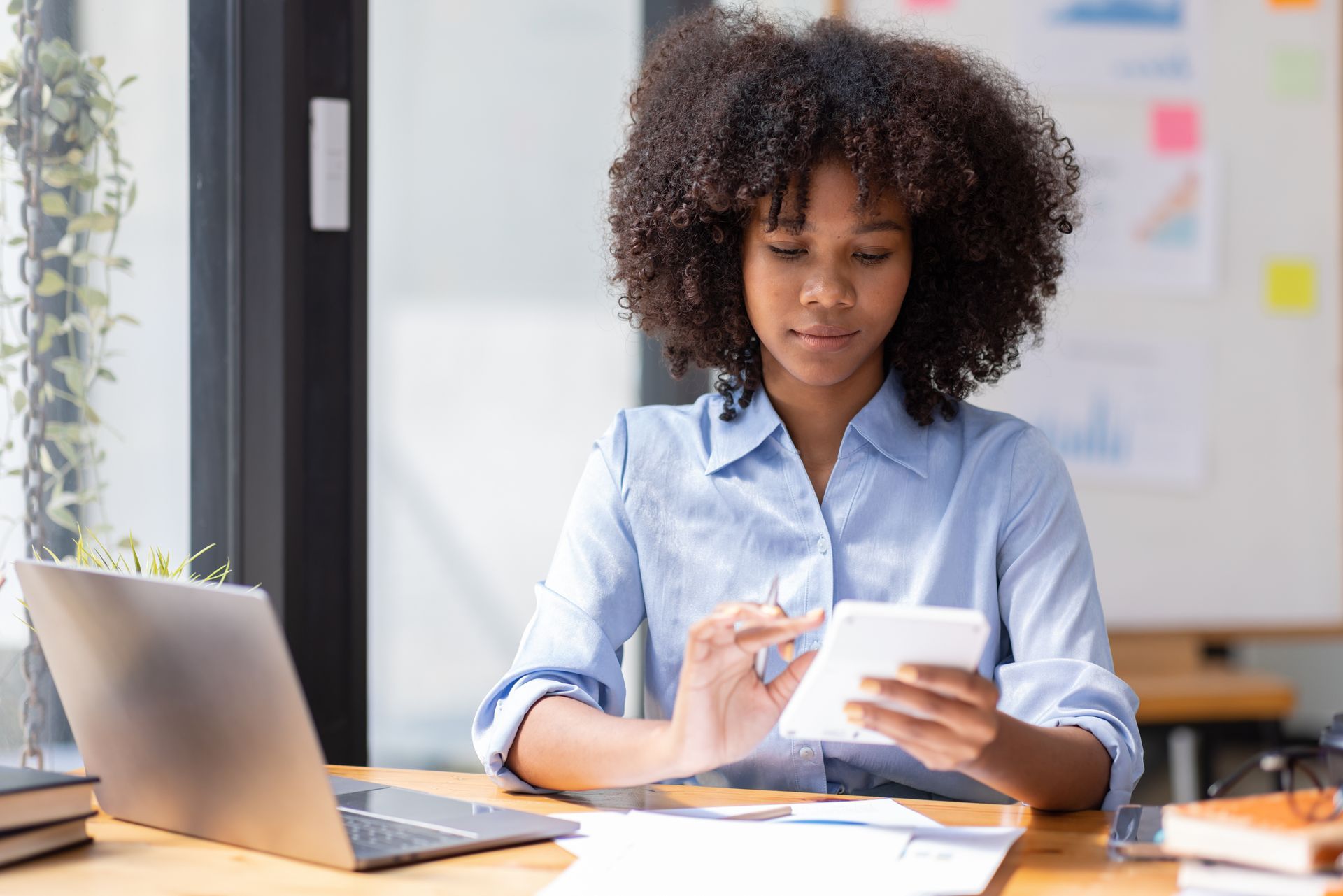 Woman using a calculator and laptop at a desk, looking focused.