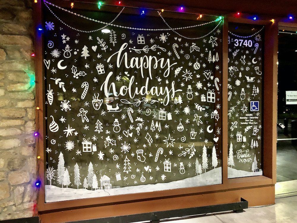 A chalkboard with christmas decorations and the words `` happy holidays '' painted on it.