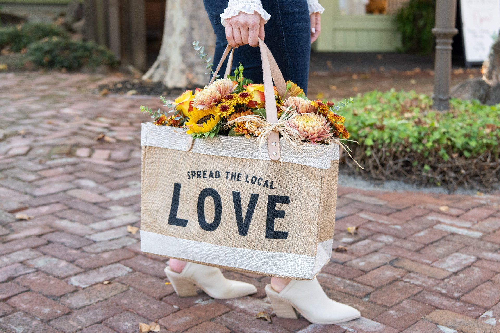 A woman is carrying a bag of flowers on a brick sidewalk.
