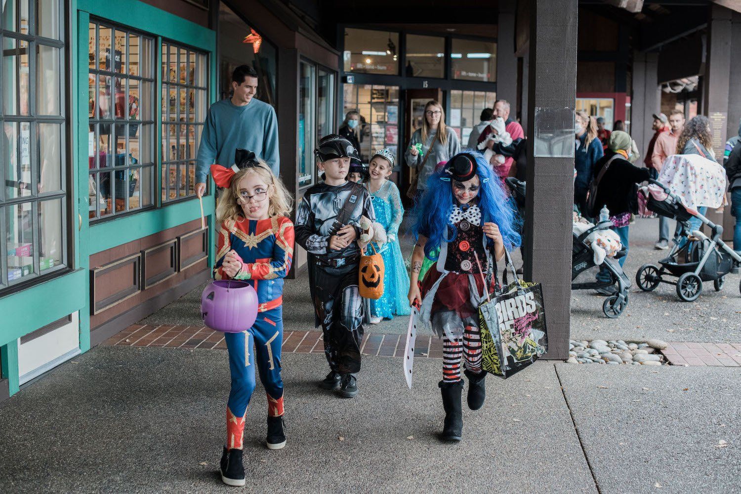 A group of children in halloween costumes are walking down a sidewalk.