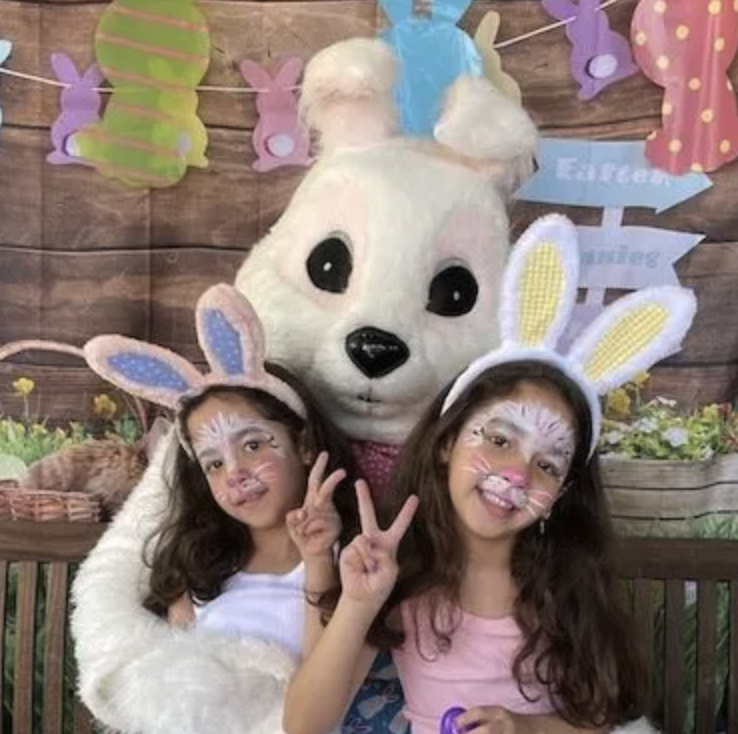 Two little girls are posing for a picture with an easter bunny mascot.