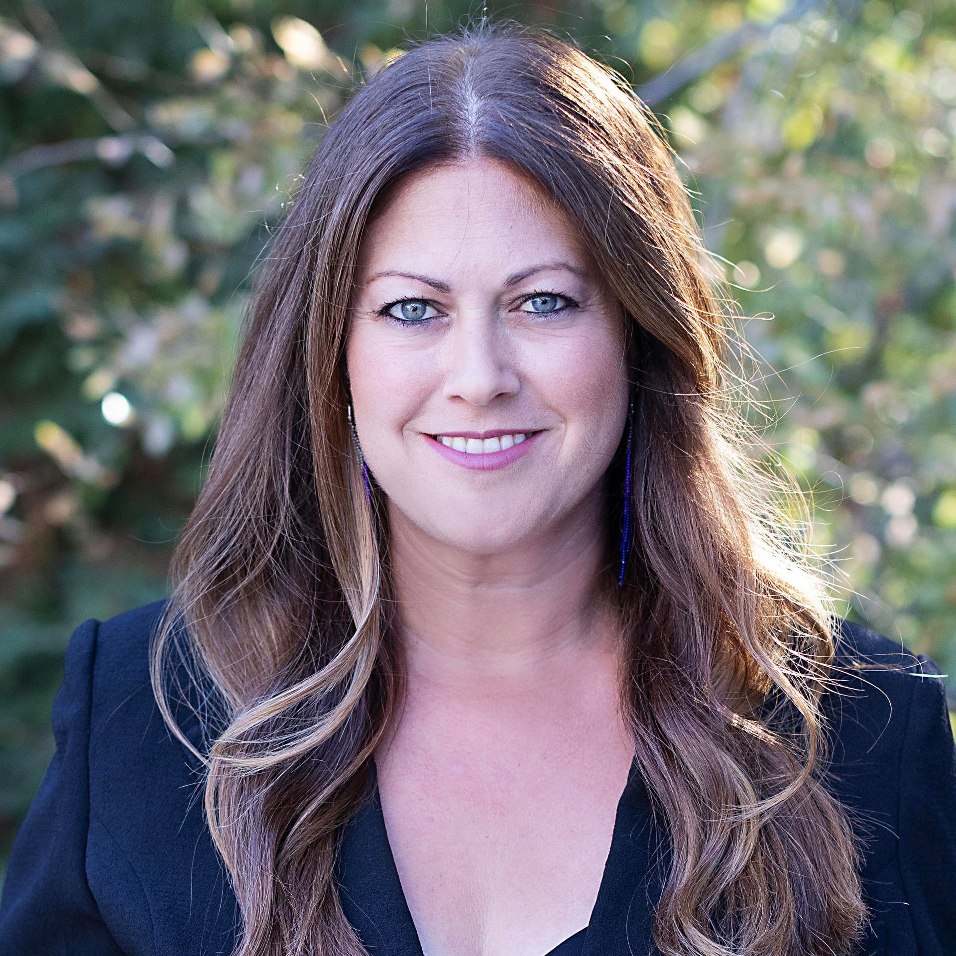 A woman with long hair is wearing a black jacket and smiling for the camera.