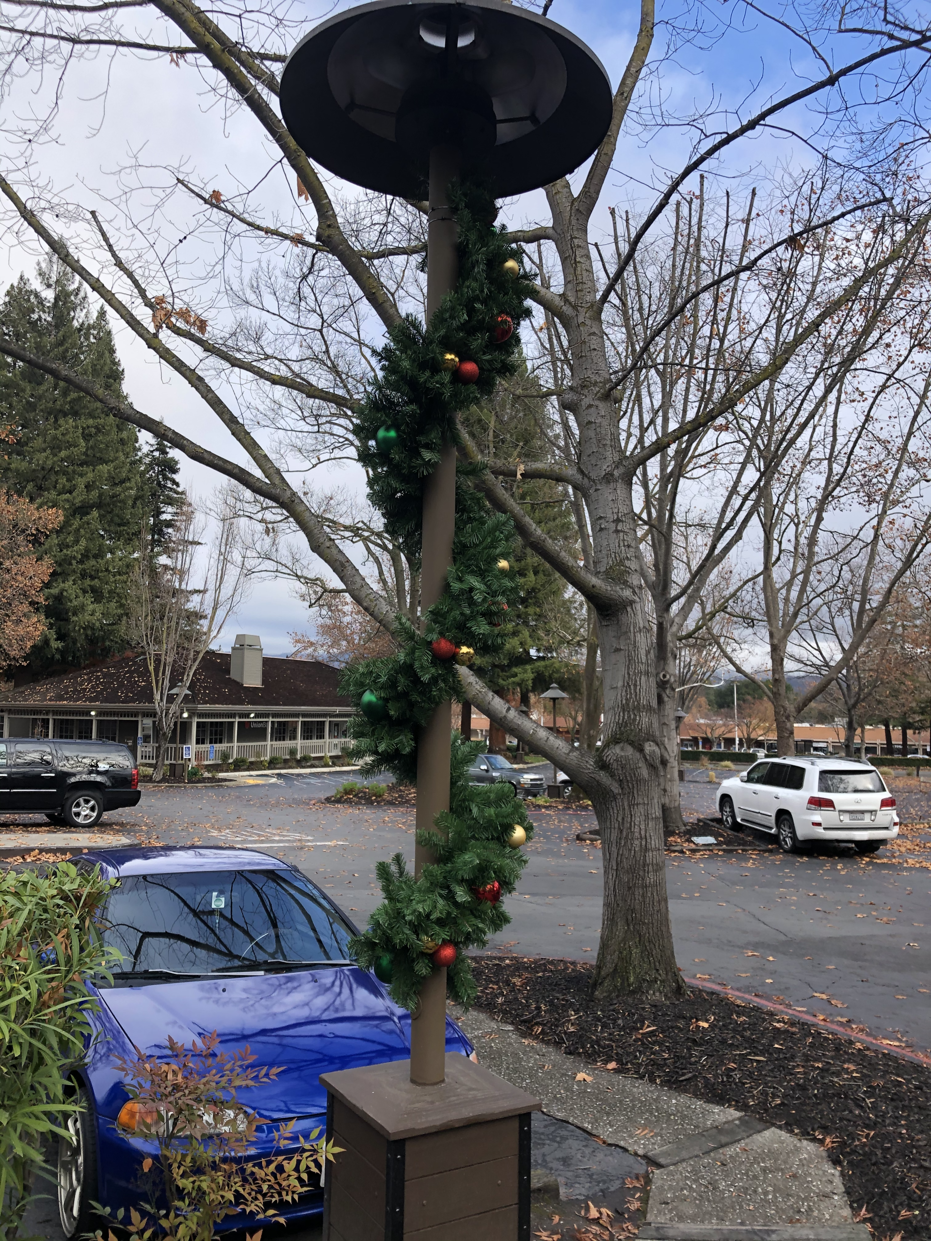 A blue car is parked next to a street light decorated for christmas