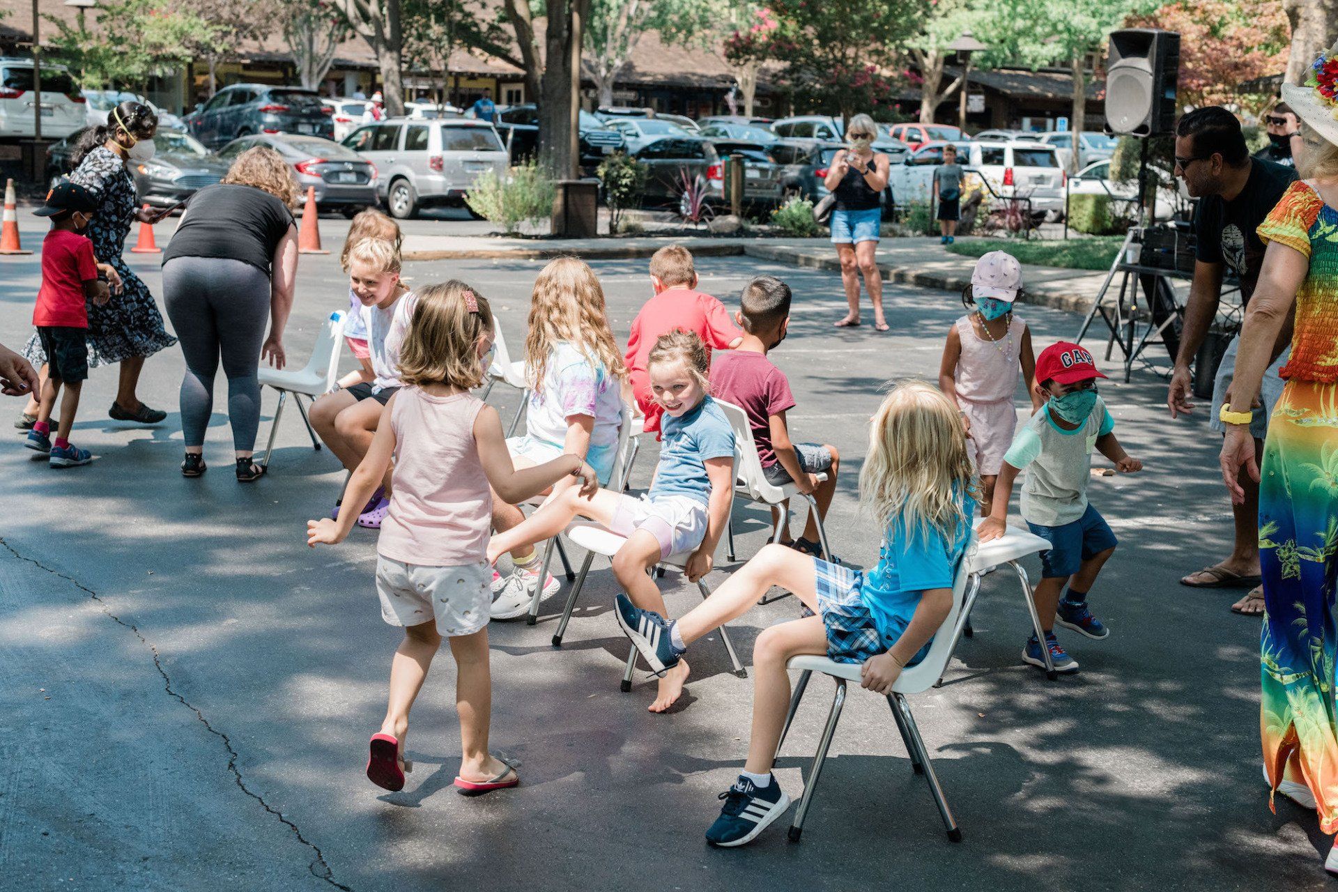 A group of children are sitting in chairs in a parking lot.