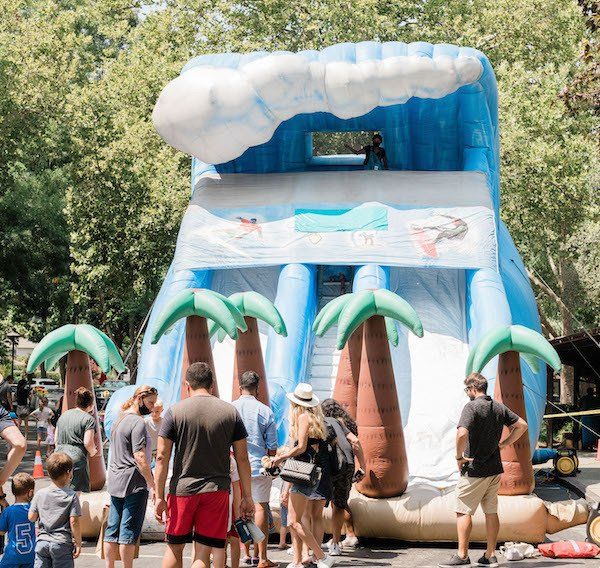 A group of people are standing around an inflatable water slide with palm trees.