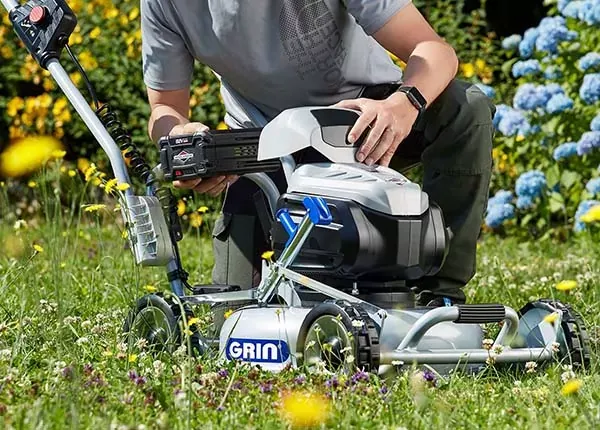 Persona che installa una batteria in un tosaerba elettrico all'aperto, in un giardino fiorito.