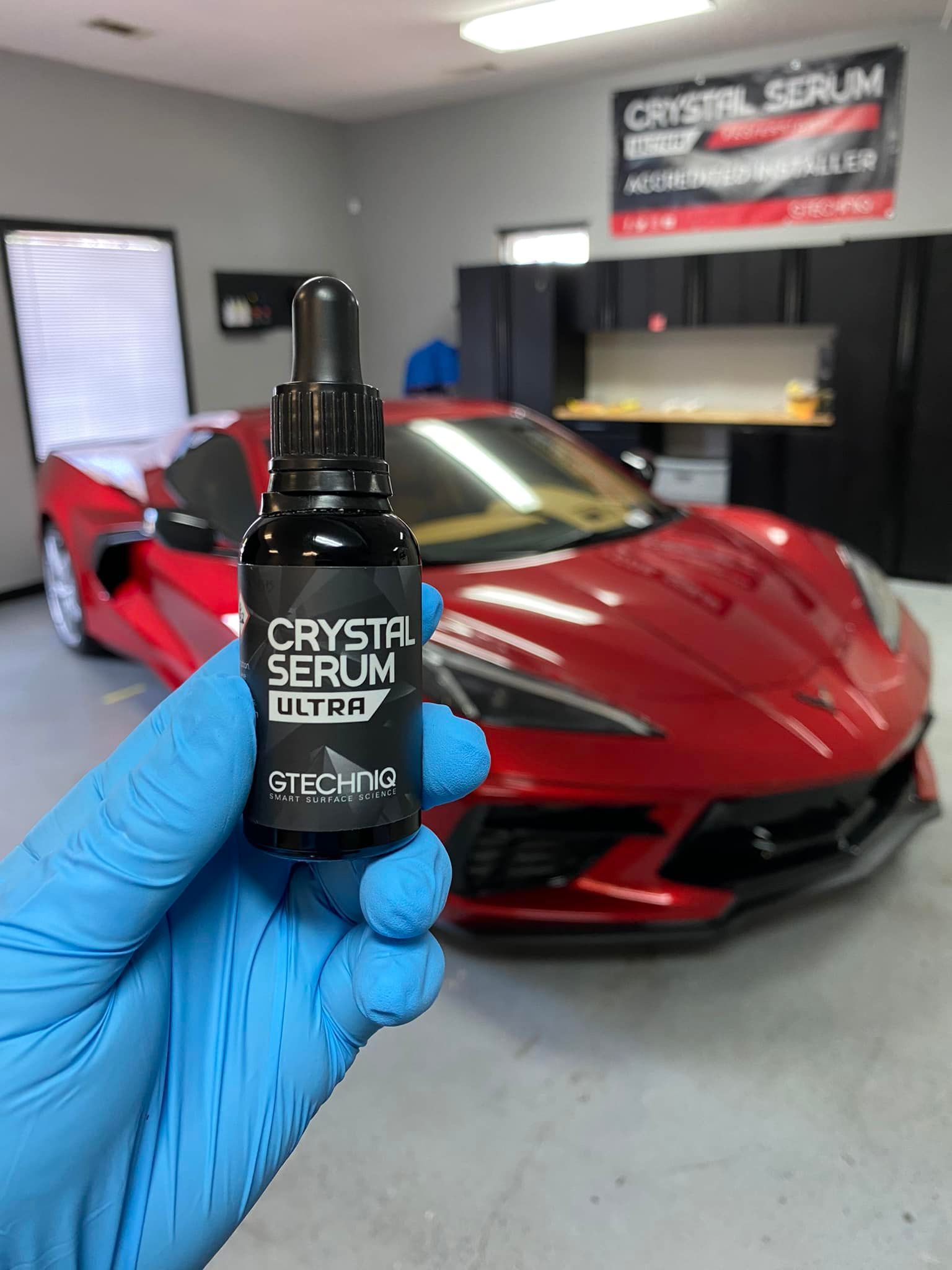 A person is holding a bottle of crystal serum in front of a red car.