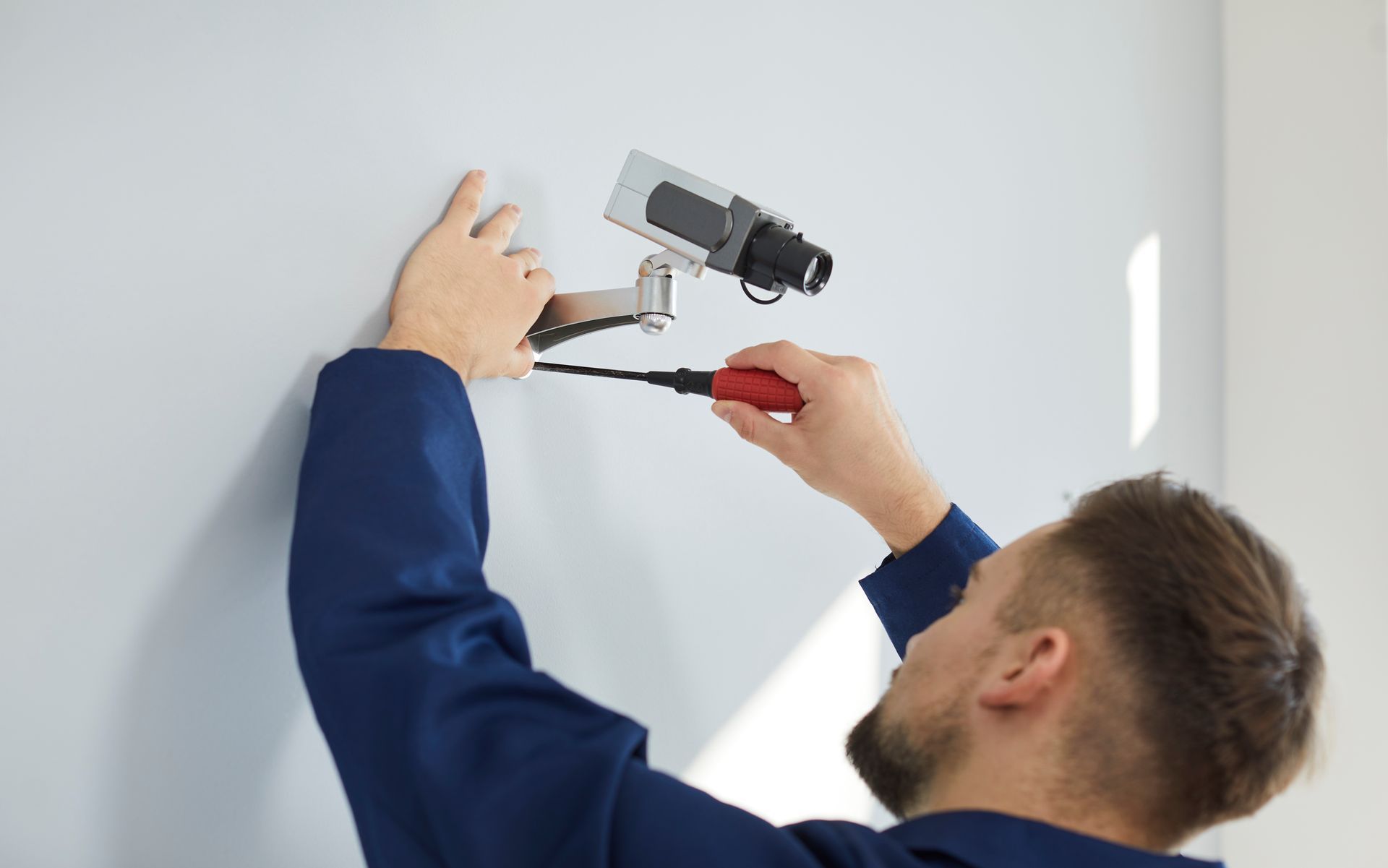 Person mounting a wall mounted security camera using a screwdriver, adjusting the bracket.