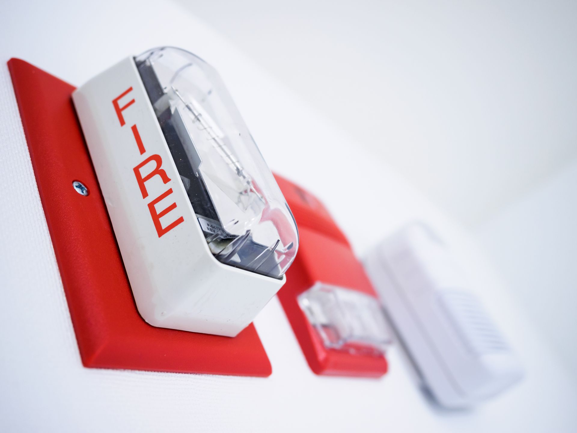 Red fire alarm strobe with bold “FIRE” text mounted on wall near smoke detector Red fire alarm strobe with bold “FIRE” text mounted on wall near smoke detector