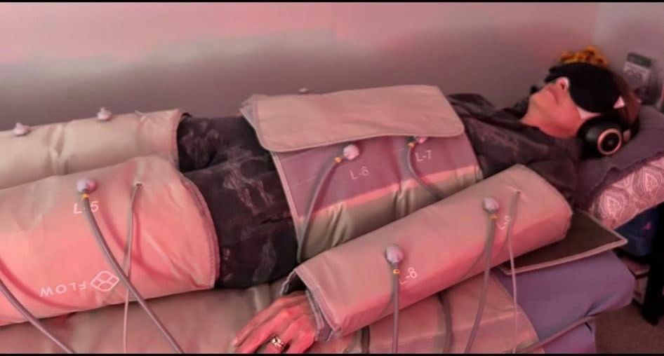 Person lying in a wellness device, eyes covered, wearing headphones.