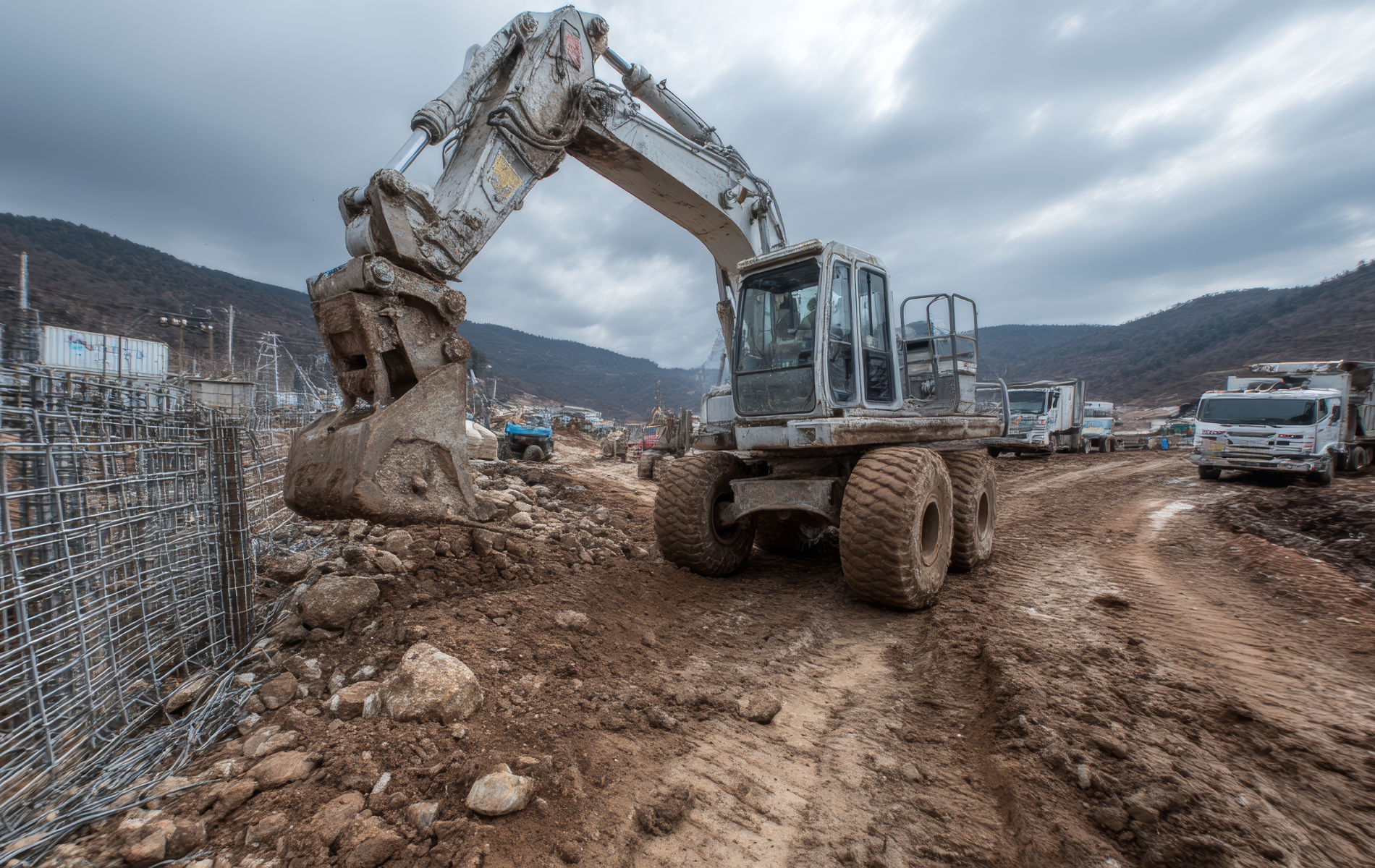 An excavator digging in a muddy construction site under an overcast sky.