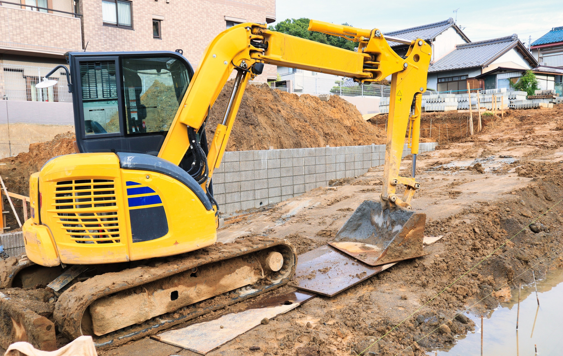 Yellow excavator digging in a muddy construction site, residential setting.