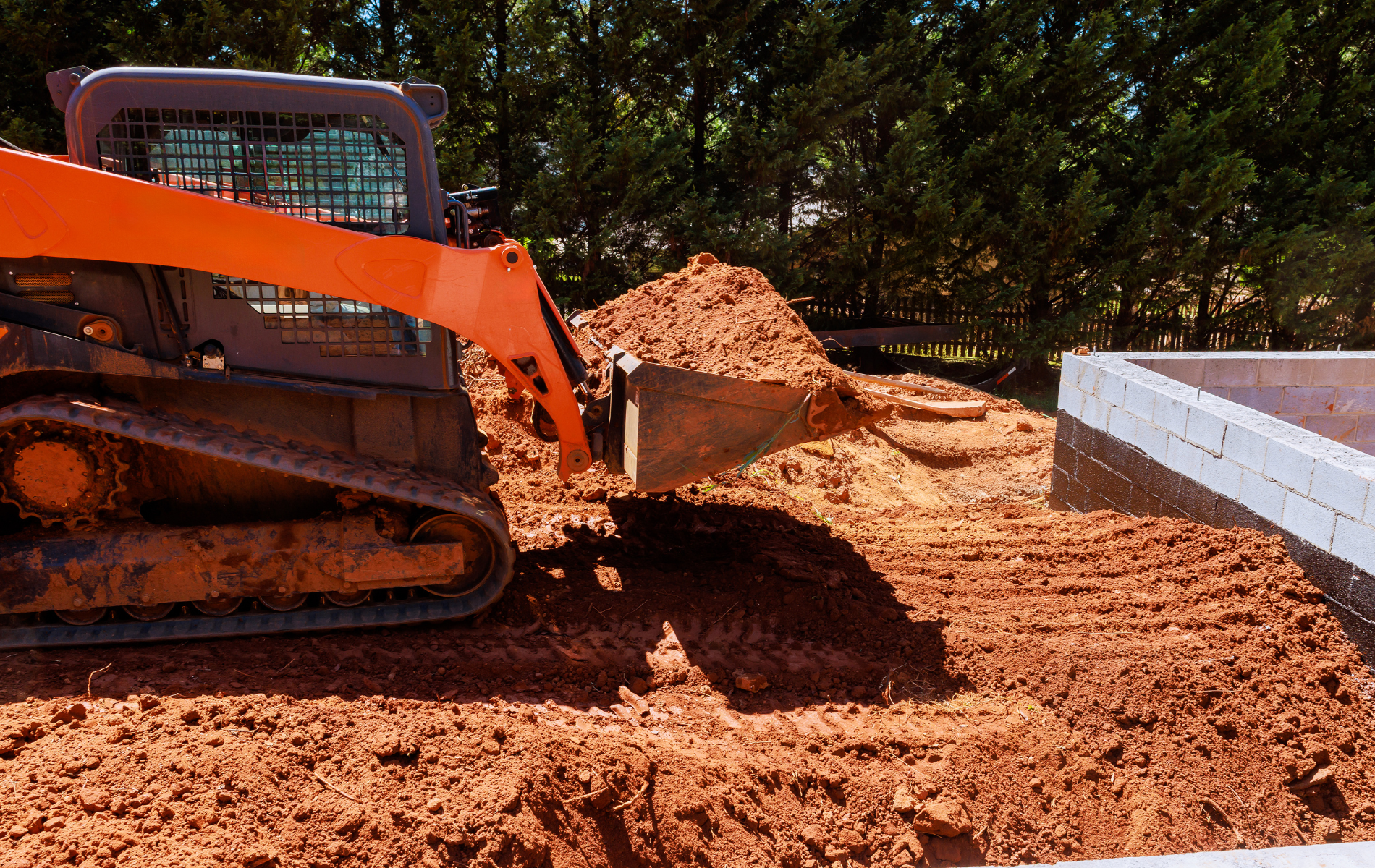 Orange skid steer moving dirt near a concrete structure outdoors.