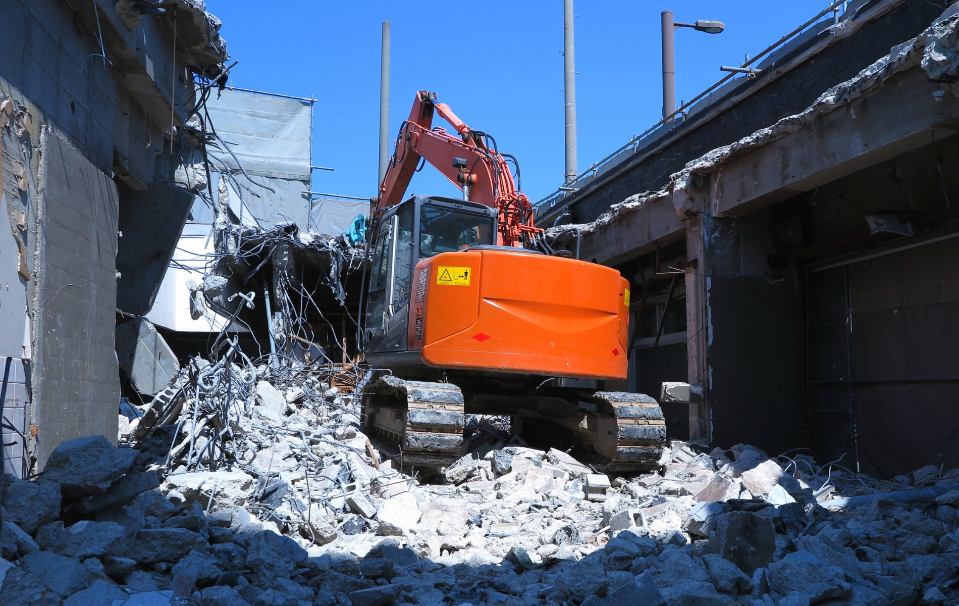 Orange excavator demolishing a building; rubble and debris surround it.