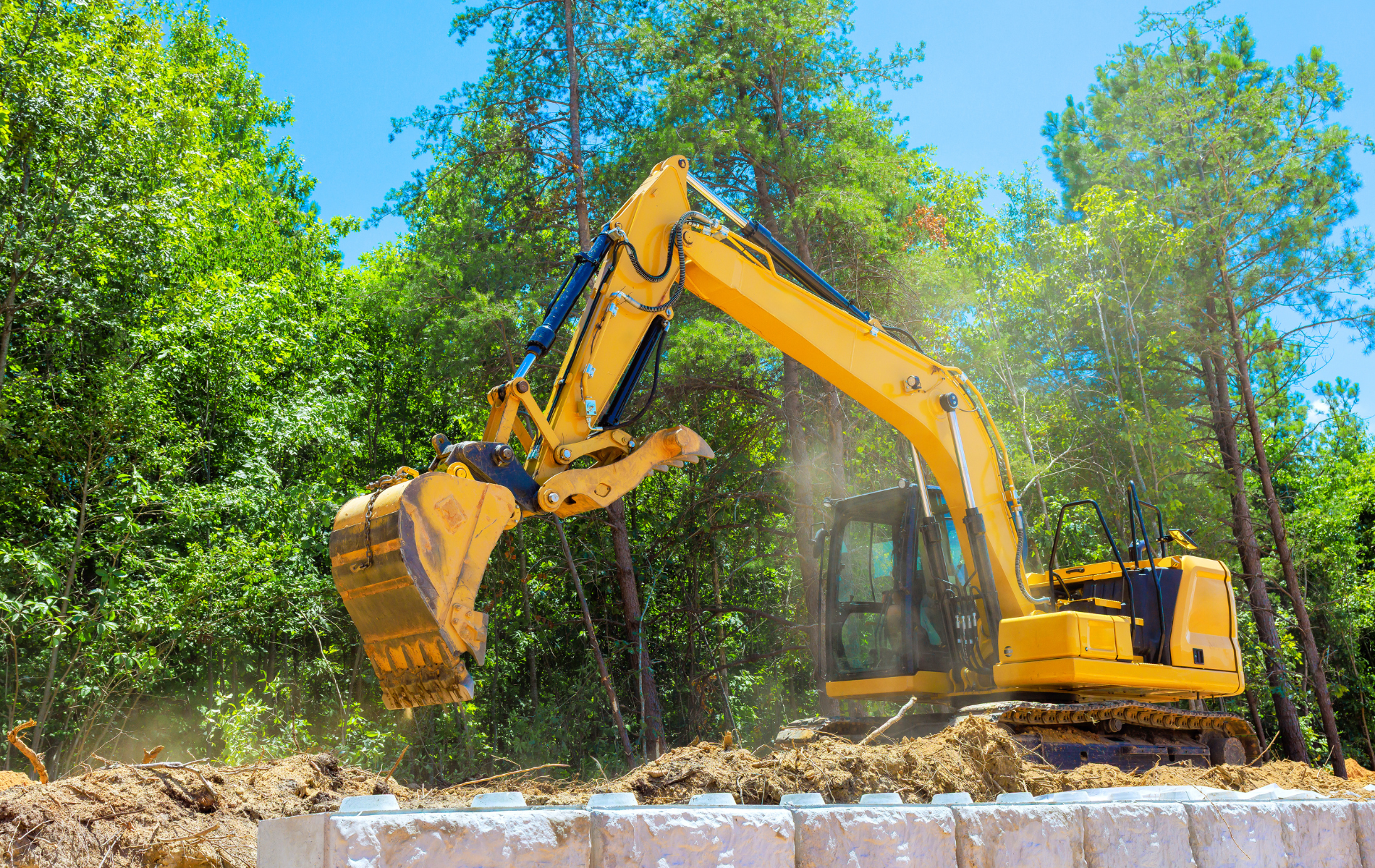 Yellow excavator digging dirt near trees on a sunny day.