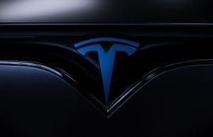 Blue Tesla logo on a dark car exterior.
