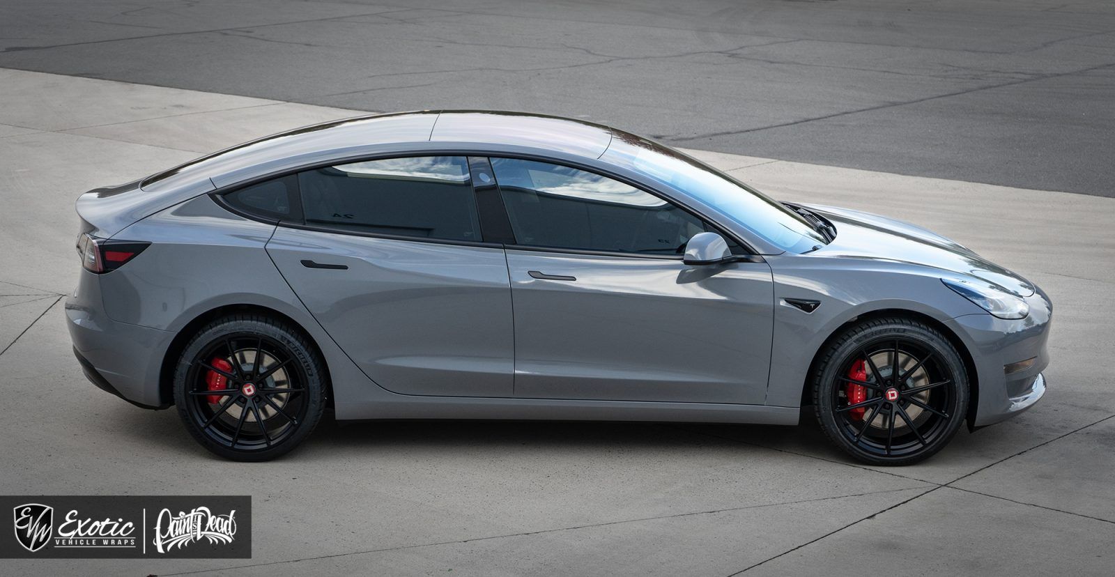 Gray Tesla Model 3 with black wheels and red brake calipers, parked on concrete.